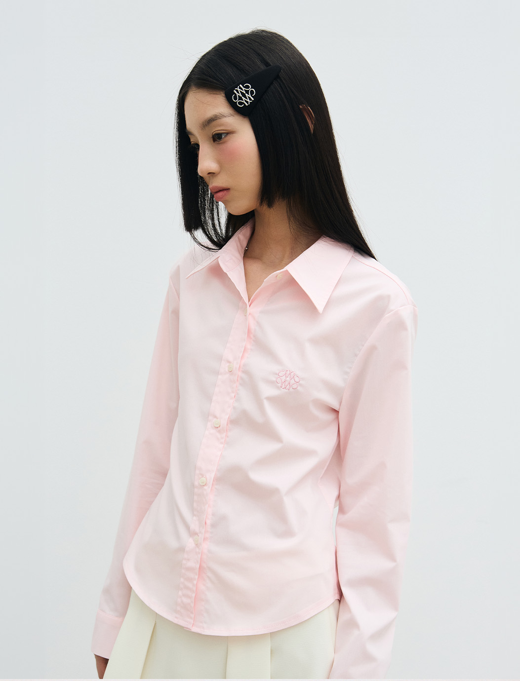 Model standing straight wearing hair clip, pink button up, and khaki skirt.